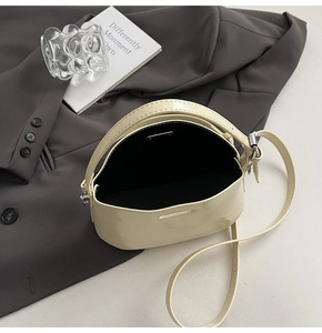 Detail shot of cream patent leather bag showing spacious black interior and long strap