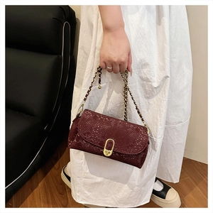 Detail of burgundy snakeskin chain bag with golden oval buckle worn over a white dress