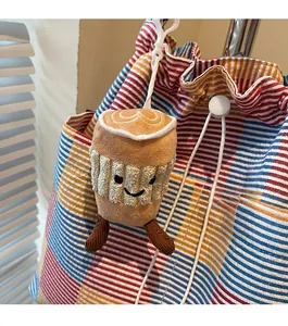 Close-up of a plush coffee cup keychain with a smiling face on a striped canvas bag