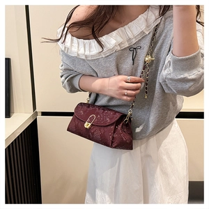 Detail of burgundy snakeskin embossed bag with gold chain strap and metal ball adjuster