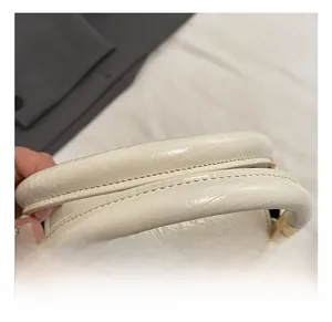Close-up of cream white handbag featuring leather texture, fine stitching and gold metal hardware