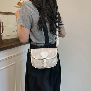 Detail of white leather trim and woven straw texture on a stylish crossbody saddle bag
