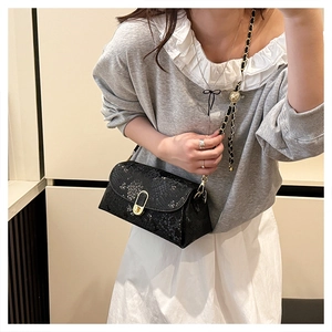 Detail of black snake pattern crossbody bag with gold chain and ball charm