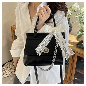 Détail du sac bandoulière en cuir verni noir avec boucle en métal et nœud en dentelle