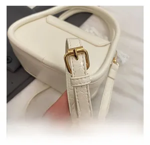 Close-up of adjustable strap with gold-tone metal buckle on cream faux leather handbag