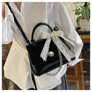 Détail du sac à main noir brillant avec fermoir argenté et nœud décoratif en dentelle blanche