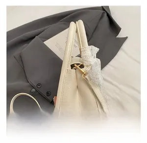 Detail of off-white textured saddle bag with gold metal hook and delicate lace bow