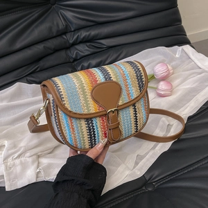 Detail of colorful woven straw saddle bag with brown leather trim and metallic buckle