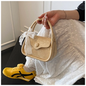 Detail of a creamy patent leather handbag with a delicate white lace bow accessory
