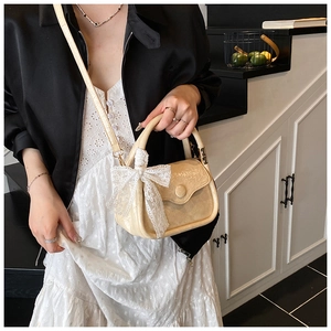 Detail of cream saddle bag featuring intricate white lace bow and textured finish