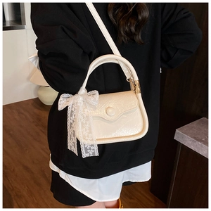 Close-up of cream saddle bag with glossy pleated texture and delicate lace bow detail