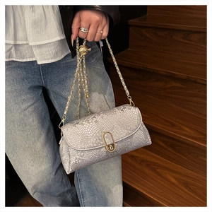 Detail of light gray snakeskin texture shoulder bag with gold chain strap on denim