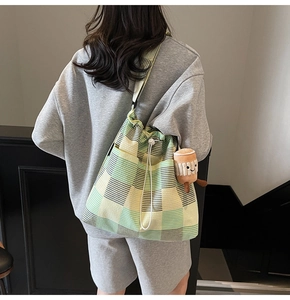 Detail of checkered canvas tote bag with drawstring closure and plush pendant on model