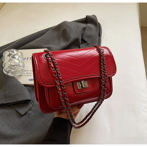 Detail of red chevron quilted crossbody bag with metal chain strap on grey blazer