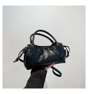 Detail of a black leather drawstring bucket bag with gold eyelets and a top handle