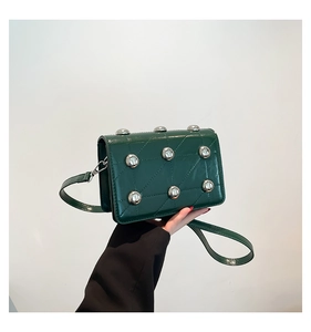 Detail of dark green quilted crossbody bag with silver rivets and metal snap closure