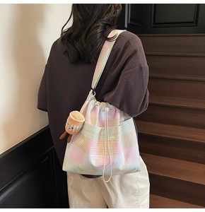 Detail view of canvas striped bucket bag with drawstring and cute plush charm on a model