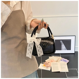Detail of black glossy saddle bag featuring a large white lace bow charm decoration