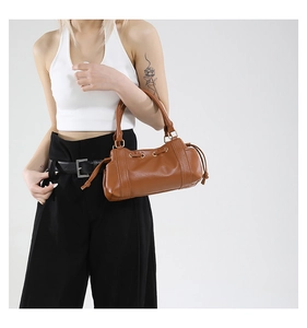Brown leather baguette bag with drawstring tassels and adjustable shoulder strap on model