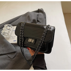 Detail of black glossy V-quilted flap bag with dark metal chain and twist lock