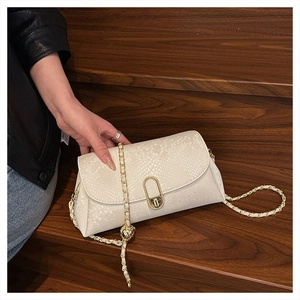 Detail of a creamy white snake-embossed crossbody bag with golden chain and twist lock