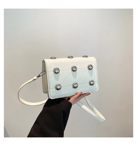 Detail of white quilted crossbody bag featuring distinctive silver metal bead accents