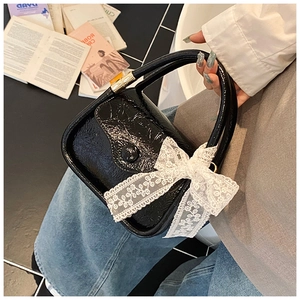 Macro shot of glossy black pleated saddle bag with contrast white lace bow detail