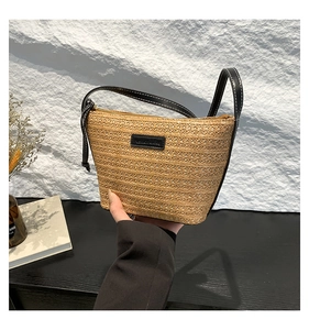Detail of hand-woven straw bucket bag featuring a black leather logo and shoulder strap