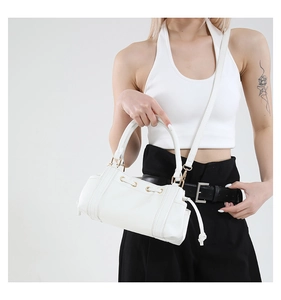 Close-up of white baguette bag featuring gold hardware and drawstring side details