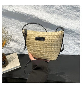 Detail of straw bucket bag with black leather trim and white stitching on a neutral background