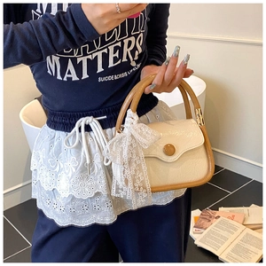 Detailed shot of a beige saddle bag with brown handles and a white lace bow accessory