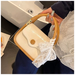 Detail of a creamy white handbag with glossy pleated texture and a large lace bow accent
