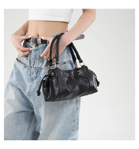 Detailed view of a black Boston handbag with gold hardware on a model in white top