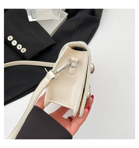 Close-up of cream crossbody bag featuring silver spherical rivets and metal buckle