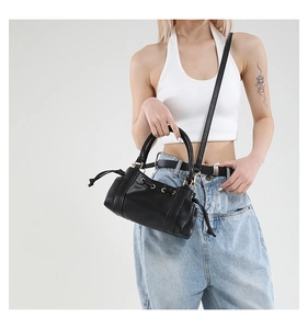 Detail of black pebbled leather crossbody bag featuring gold hardware and drawstring closure