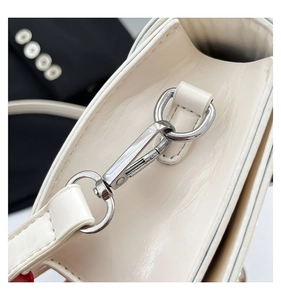 Close-up of shiny silver metal lobster clasp and textured beige leather shoulder bag