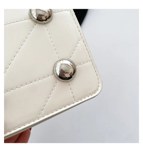 Close-up of white quilted handbag featuring silver studs and high-gloss stitching texture
