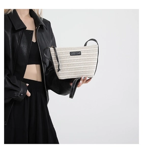 Detail of a woven straw crossbody bag with black leather straps on a model wearing black