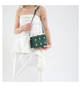 Detail of dark green quilted leather bag with silver rivets and sleek metallic finish