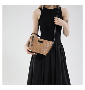 Detail of woven straw crossbody bag with brown textures and black leather brand tag
