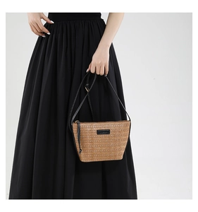 Detail view of straw crossbody bag with black leather strap and golden hardware