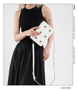 White quilted crossbody bag with large silver rivets shown on a model in a black dress