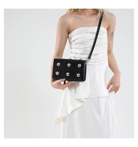 Close-up of black quilted crossbody bag with silver sphere studs on white dress
