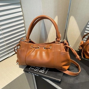 Brown drawstring handbag with metal eyelets and side pockets on a minimalist prop background