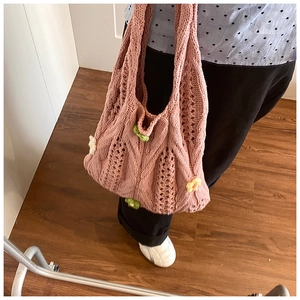 Detailed close-up of pink knit shoulder bag with woven floral appliques and hollow texture