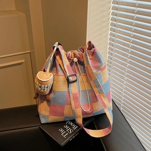 Colorful plaid canvas bucket bag with drawstring closure and adjustable strap on a leather sofa