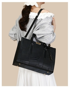 Detail of large black crocodile pattern tote bag with gold metal plate and protective feet