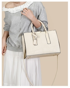 Detail of off-white crocodile embossed tote bag featuring sturdy handles and leather tag
