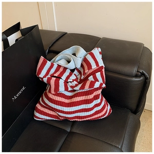 Detailed close-up of a striped knit tote bag in red, pink, and light blue on a sofa