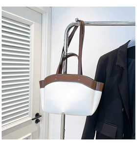Side view of white and brown bicolor tote bag with leather texture hanging on a metal stand